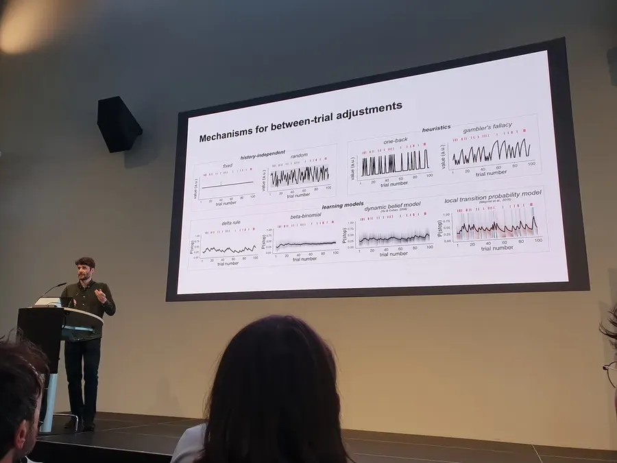 A lab member presents a slide comparing learning models of between-trial adjustments at a conference.