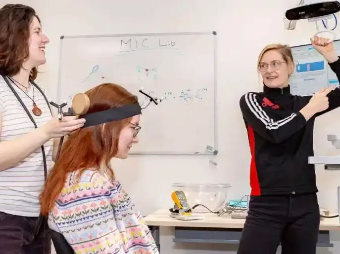A researcher holds a stimulation transducer to a participant's head while a colleague points at brain images on the neuronavigation screens.